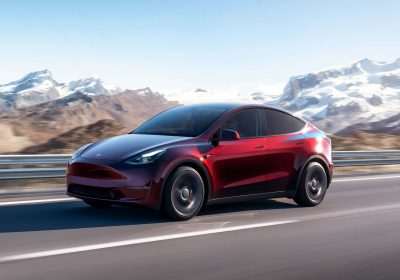 红色特斯拉 Model Y 在山间公路上行驶，展示辅助驾驶车型外观