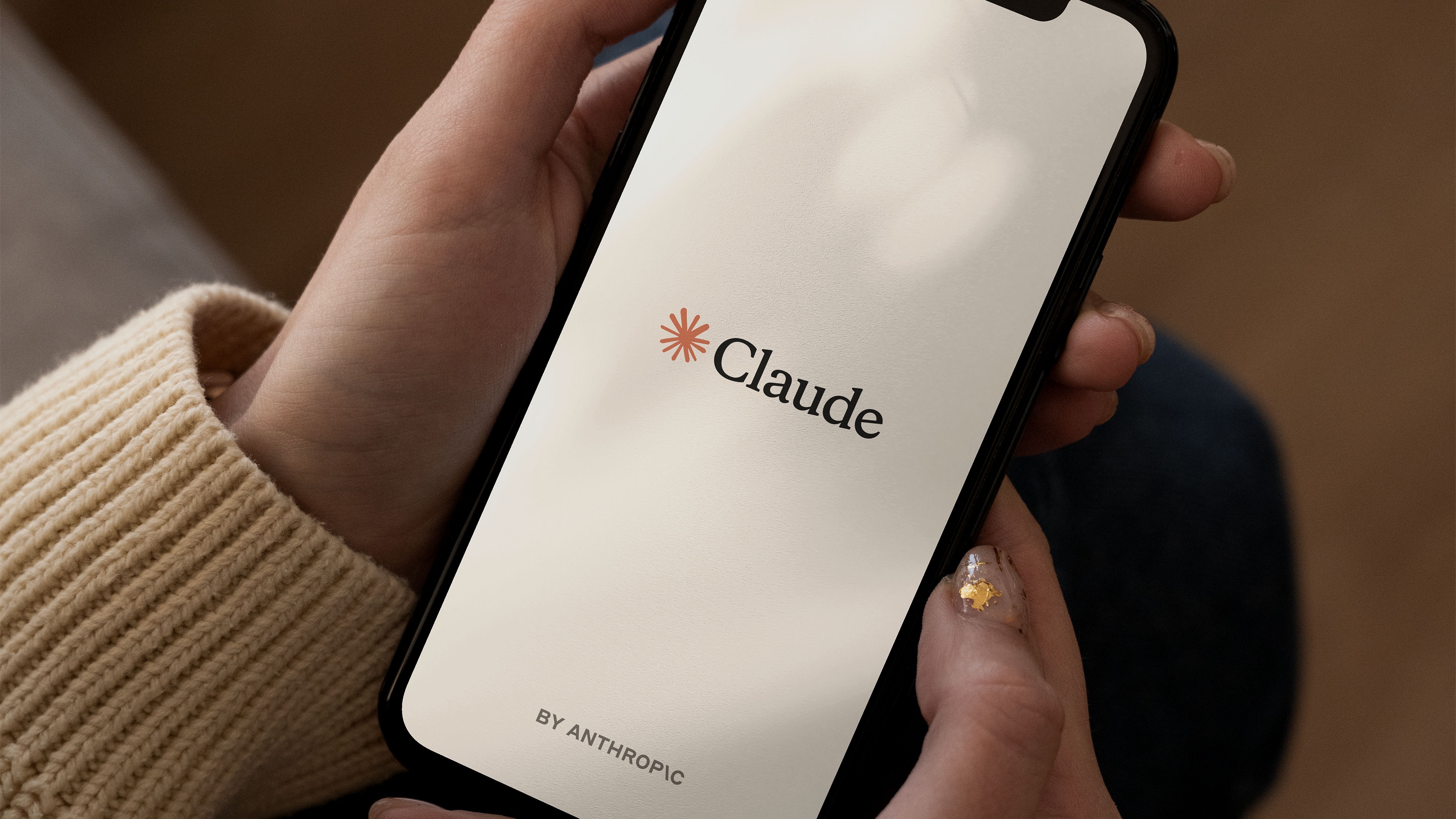 双手捧着显示 Claude 启动页面的智能手机